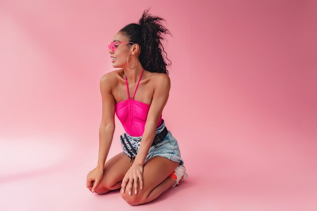 zwarte afro-amerikaanse vrouw zit in een stijlvolle zomeroutfit roze top en korte broek heuptas op roze