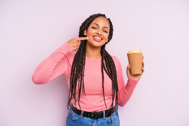 Zwarte afrovrouw die vol vertrouwen glimlacht en naar eigen brede glimlach wijst. koffie meenemen