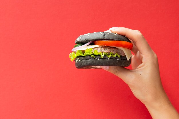 Zwarte hamburger die voor rode achtergrond wordt gehouden