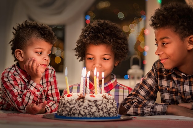Zwarte kinderen met verjaardagstaart drie jongens aan verjaardagstafel gelukkige verjaardag broer kijken naar de c...