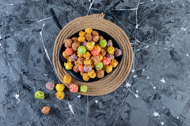 Zwarte kom kleurrijke smakelijke popcorns op marmeren oppervlak.