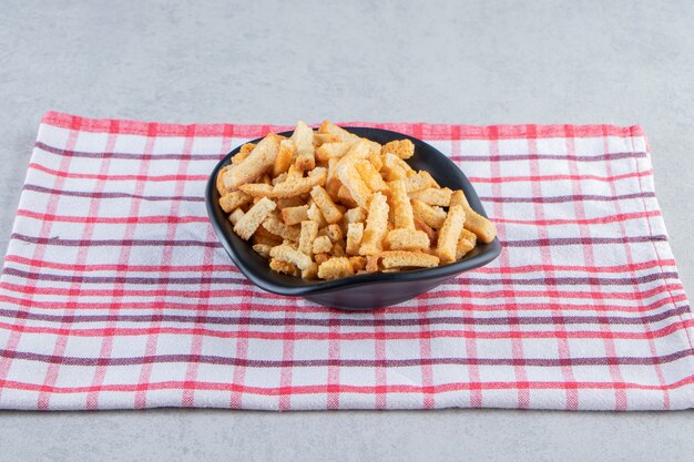 Zwarte kom smakelijke knapperige crackers op stenen achtergrond.