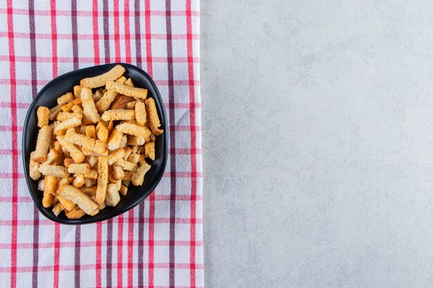 Zwarte kom smakelijke knapperige crackers op stenen achtergrond.