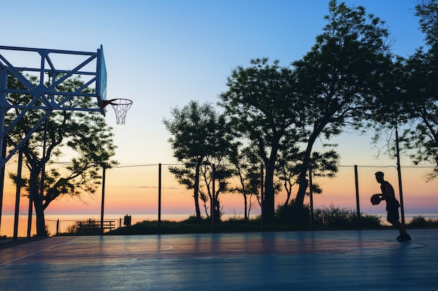 Gratis foto zwarte man sport doen, basketbal spelen op zonsopgang, silhouet