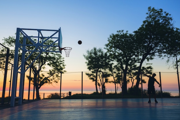 Zwarte man sport doen, basketbal spelen op zonsopgang, silhouet