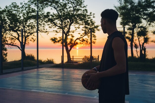 Zwarte man sport doen, basketbal spelen op zonsopgang, silhouet