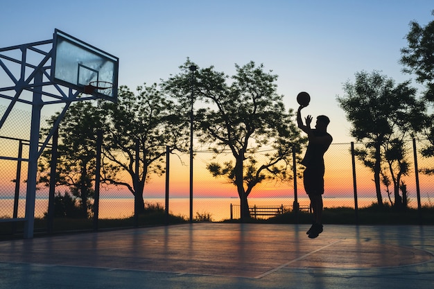 Gratis foto zwarte man sporten, basketbal spelen op zonsopgang, silhouet springen