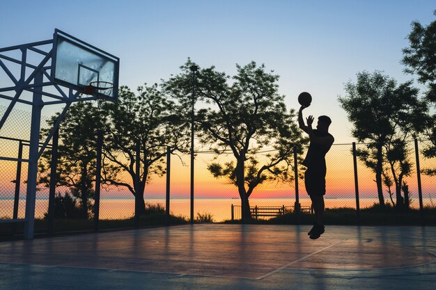 Zwarte man sporten, basketbal spelen op zonsopgang, silhouet springen