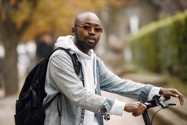 Zwarte man staande op een straat met elektrische scooter. Man met witte hoodie en zwarte spijkerbroek