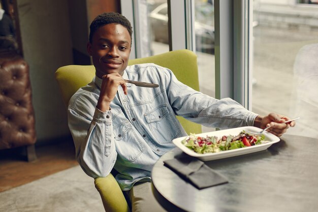 Zwarte man zit in een cafe en het eten van een groente salade