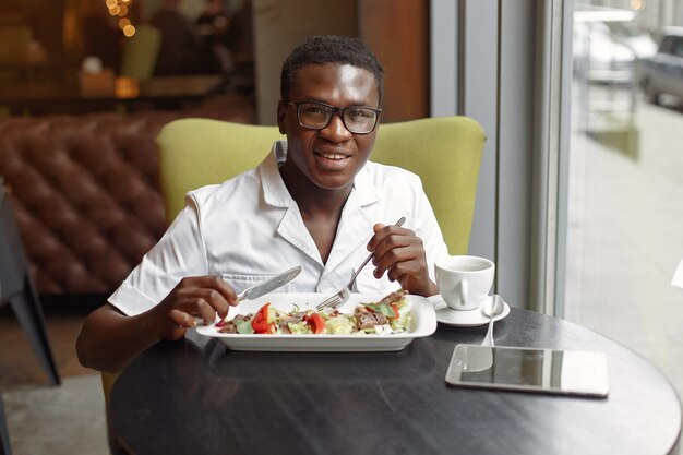 Zwarte man zit in een cafe en het eten van een groente salade