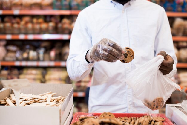 Zwarte mens die koekjes in plastic zak in kruidenierswinkel zetten
