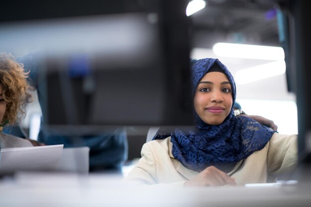 Zwarte moslim vrouwelijke softwareontwikkelaar werkt samen met haar multi-etnische business team met behulp van computer tijdens het schrijven van programmeercode op modern startup-kantoor