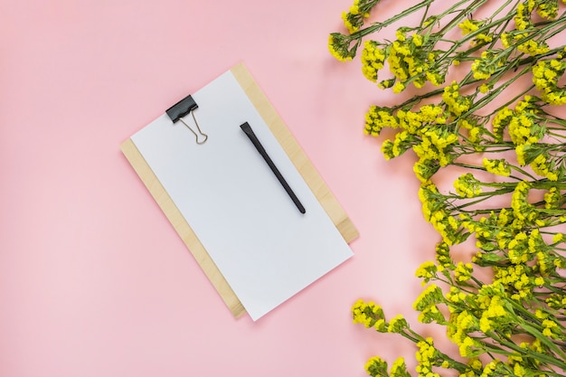 Zwarte pen op papier over houten klembord en gele bloemen tegen roze achtergrond