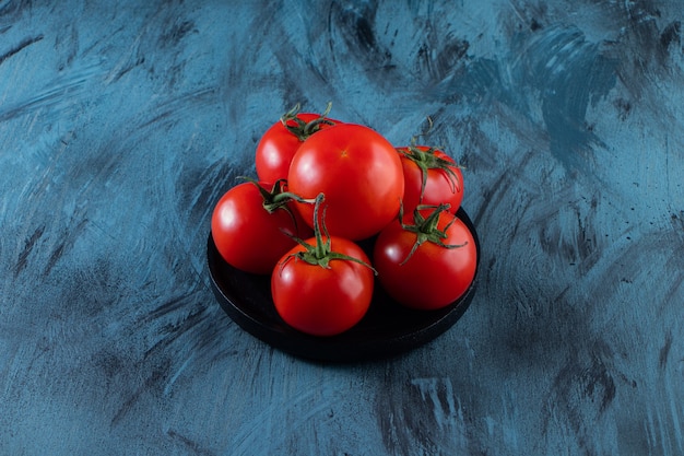 Zwarte plaat van rode verse tomaten op blauwe ondergrond.