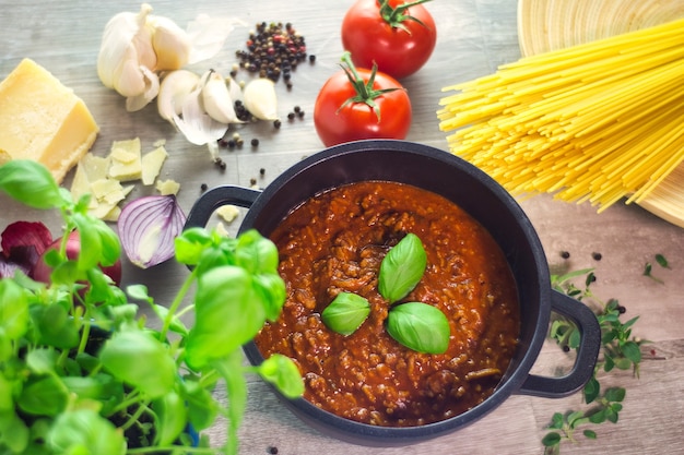 Zwarte pot kooksaus bolognese met ingrediënten op een houten tafel