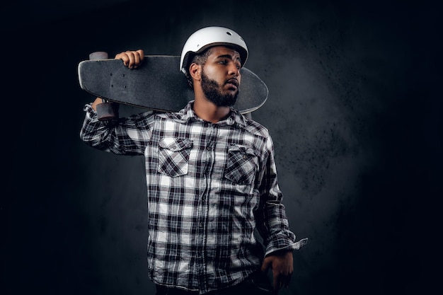 Zwarte skater gekleed in een fleece shirt houdt lang bord over grijze achtergrond in een studio.