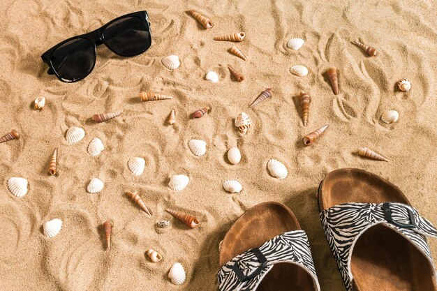 Zwarte slippers en zonnebril, zeeschelp op zand. Met plaats voor uw tekst. Bovenaanzicht. Ruimte kopiëren. Stillevenmodel plat gelegd