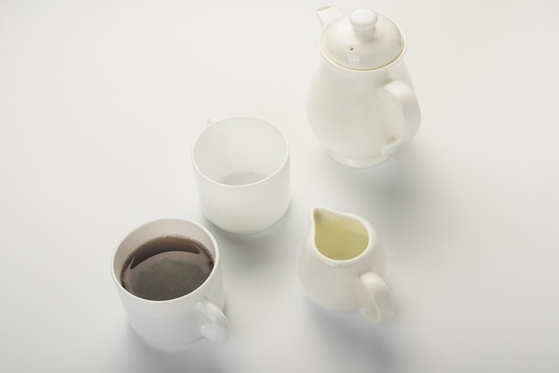 Zwarte thee; melkkan; witte kop en theepot geïsoleerd op een witte achtergrond