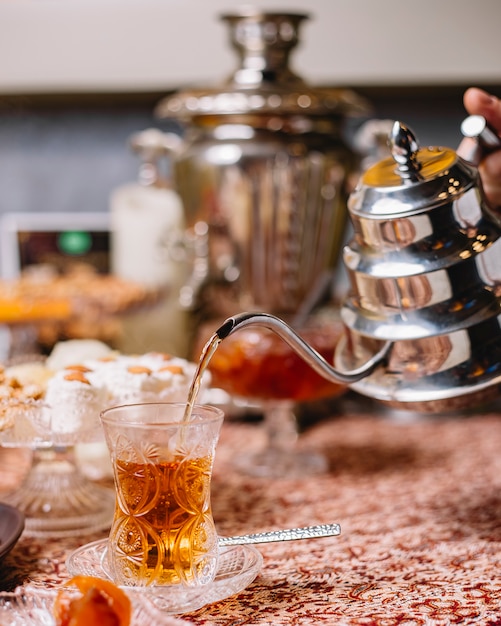 Zwarte thee wordt uit een stalen theepot in kristalarmudu-glas gegoten