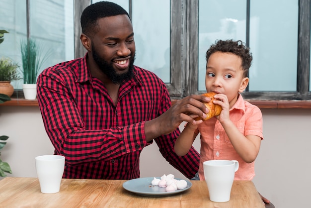 Gratis foto zwarte vader voedende zoon met croissant