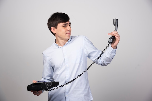Zwarte vaste telefoon in de hand van een man op grijze muur.